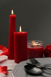 Romantic place setting with red candles and rose on wooden table, closeup. St. Valentine's day dinner