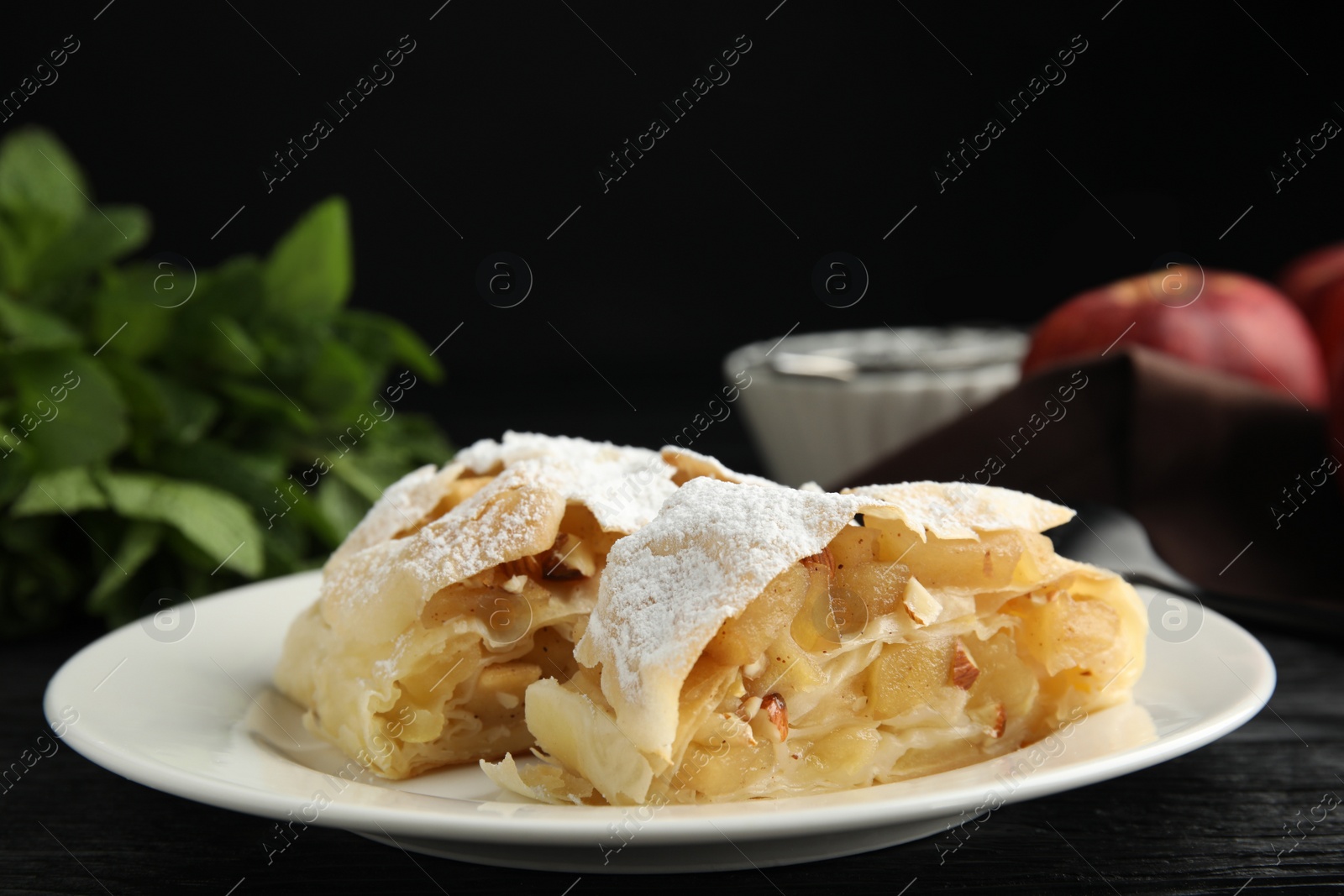 Photo of Delicious apple strudel with almonds and powdered sugar on black wooden table, closeup. Space for text