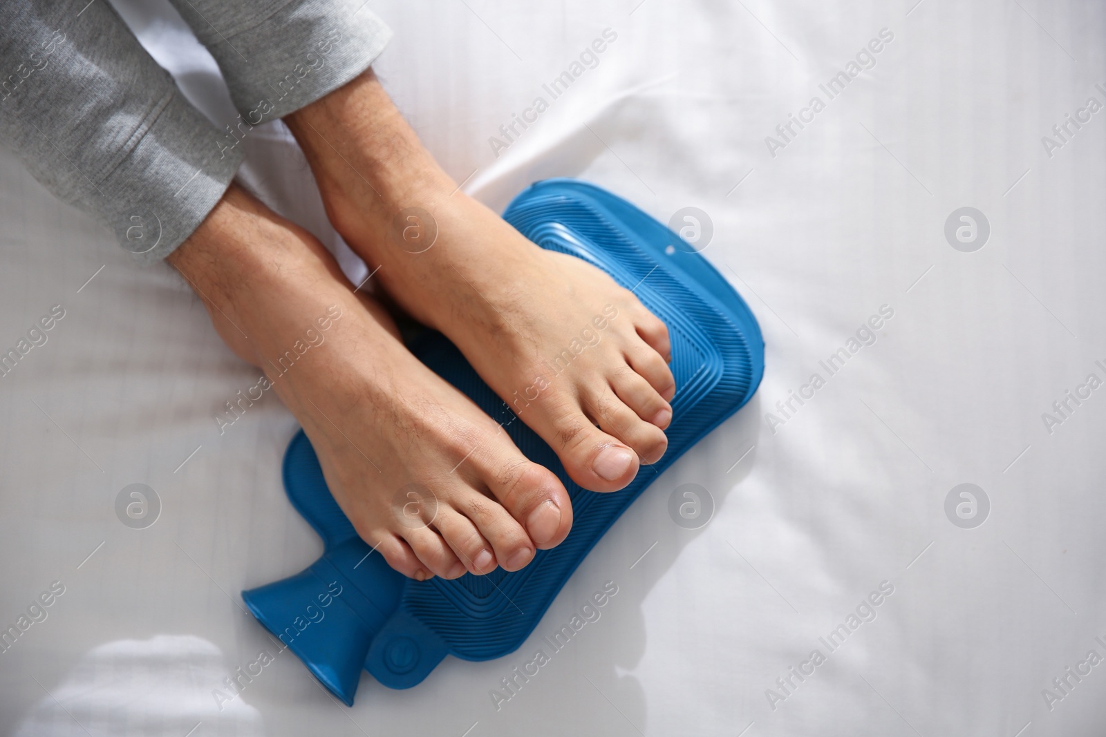 Photo of Man warming feet with hot water bottle on bed, closeup