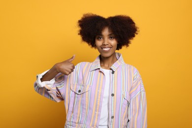 Smiling African American woman showing thumbs up on orange background