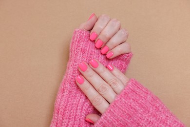 Photo of Woman showing her manicured hands with pink nail polish on dark beige background, closeup