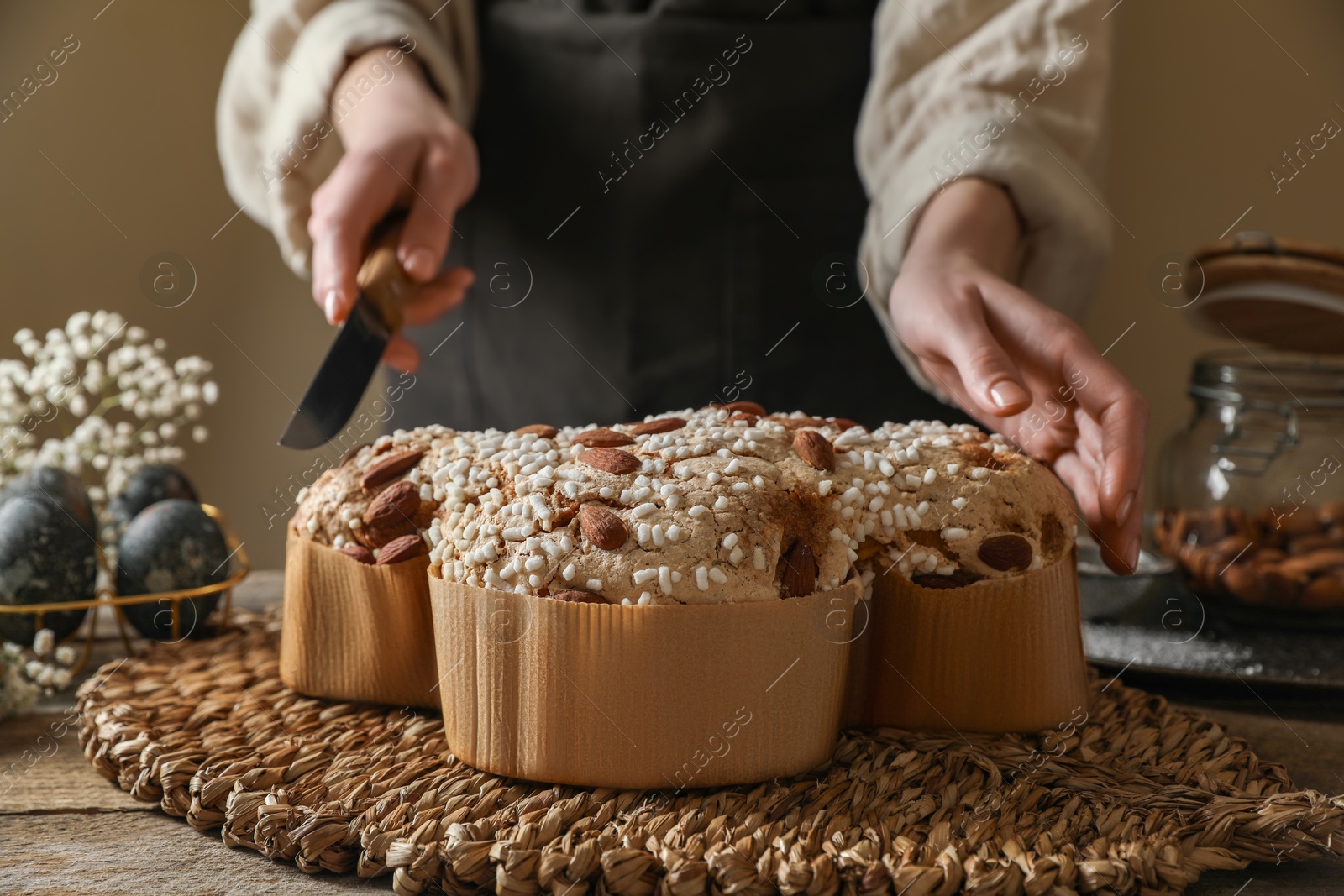 Photo of Woman cutting delicious Italian Easter dove cake (traditional Colomba di Pasqua) at wooden table, closeup