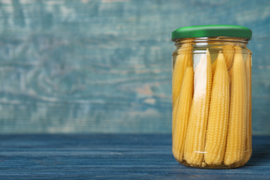 Photo of Glass jar of pickled corn cobs on blue wooden table. Space for text