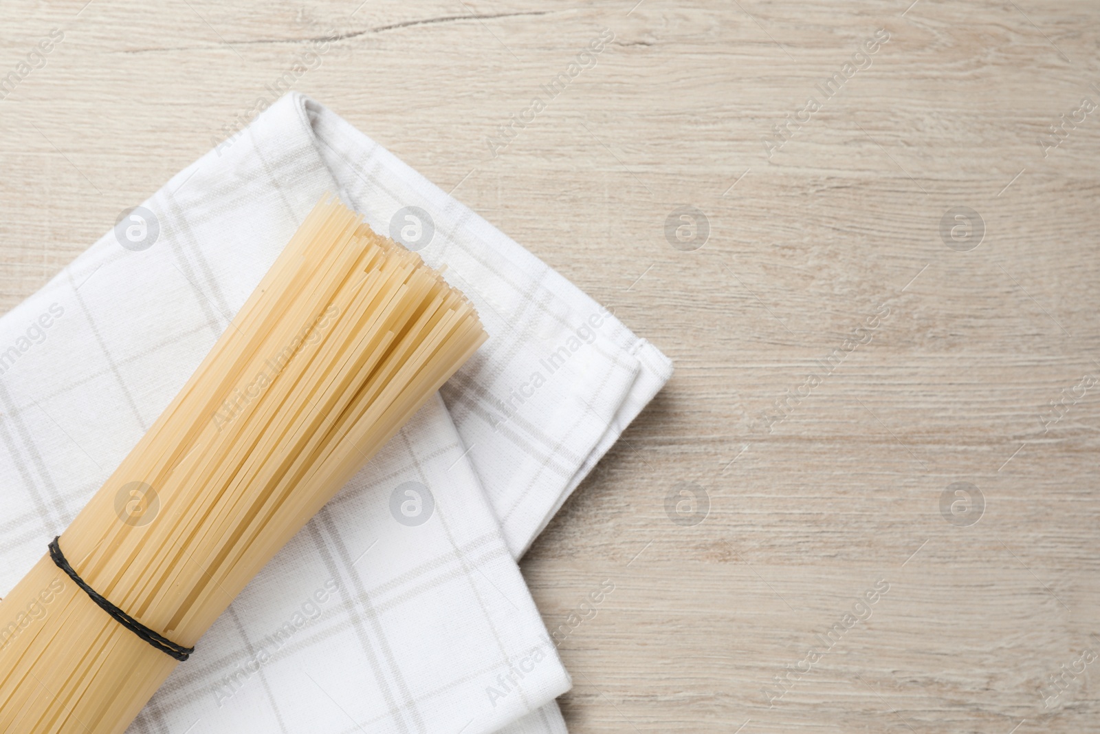 Photo of Uncooked rice noodles with napkin on wooden table, top view. Space for text