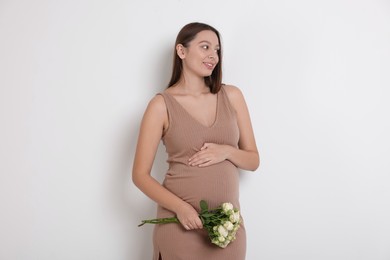 Photo of Beautiful pregnant woman in beige dress with bouquet of roses on white background