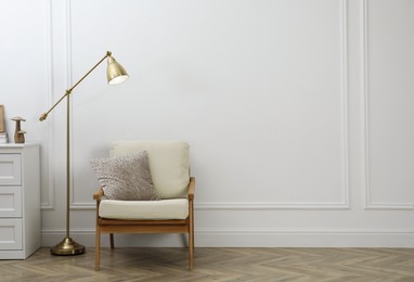 Photo of Stylish room interior with lamp, chest of drawers and armchair near white wall. Space for text