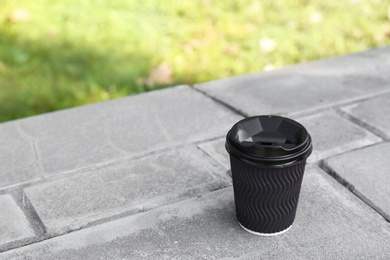 Photo of Cardboard coffee cup on stone parapet outdoors. Space for text