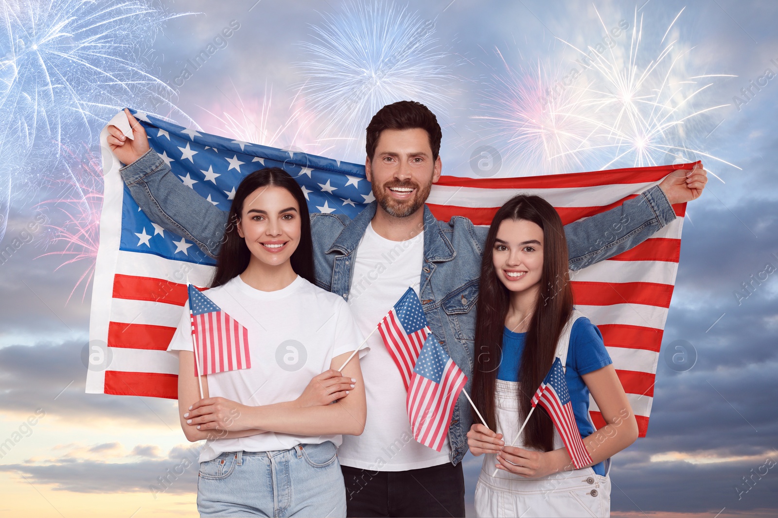 Image of 4th of July - Independence day of America. Happy family holding national flags of United States against sky with fireworks