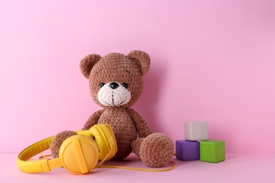 Photo of Baby songs. Toy bear, headphones and cubes on pink background