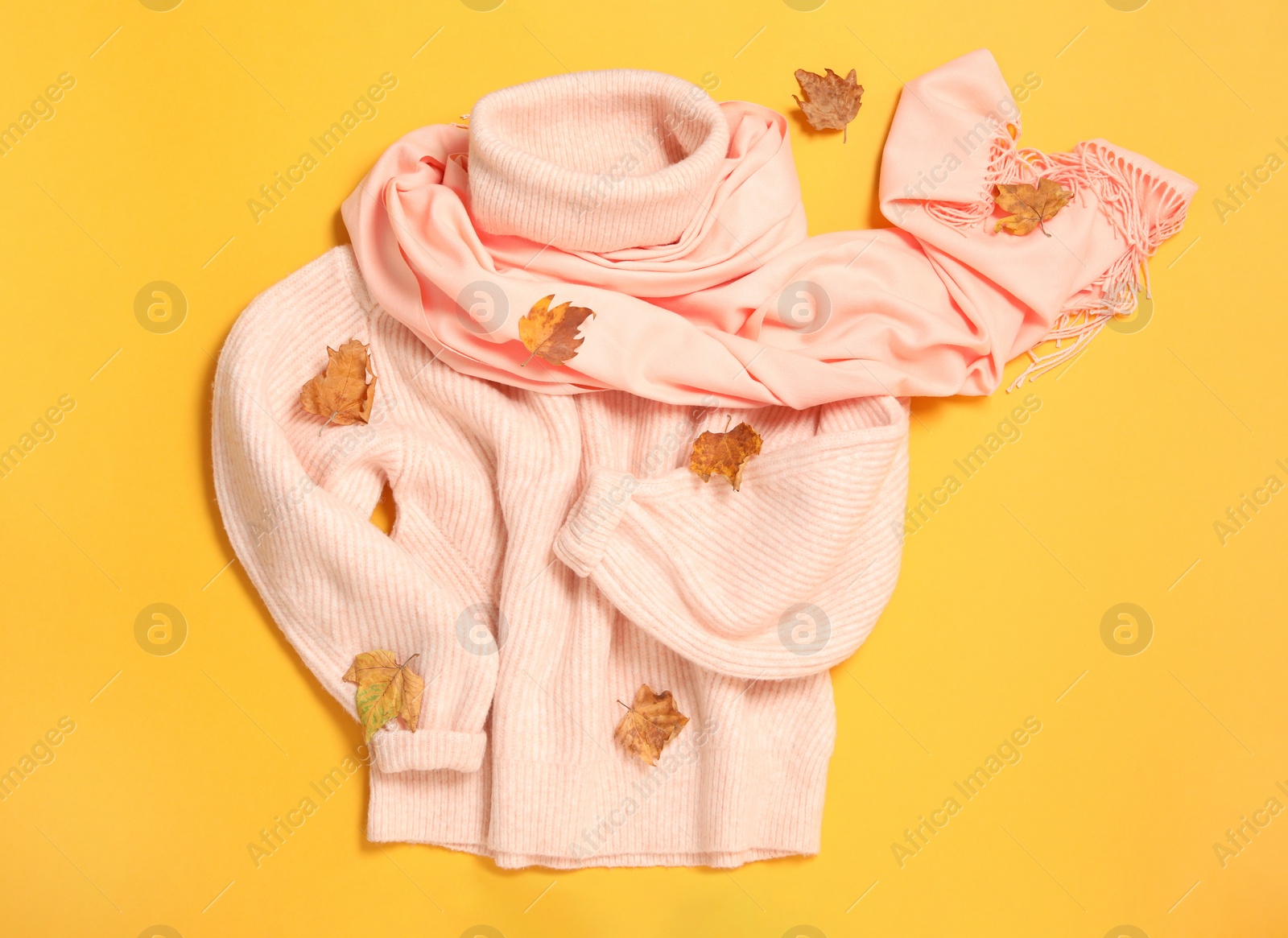 Photo of Pink sweater, scarf and dry leaves on yellow background, flat lay. Autumn season
