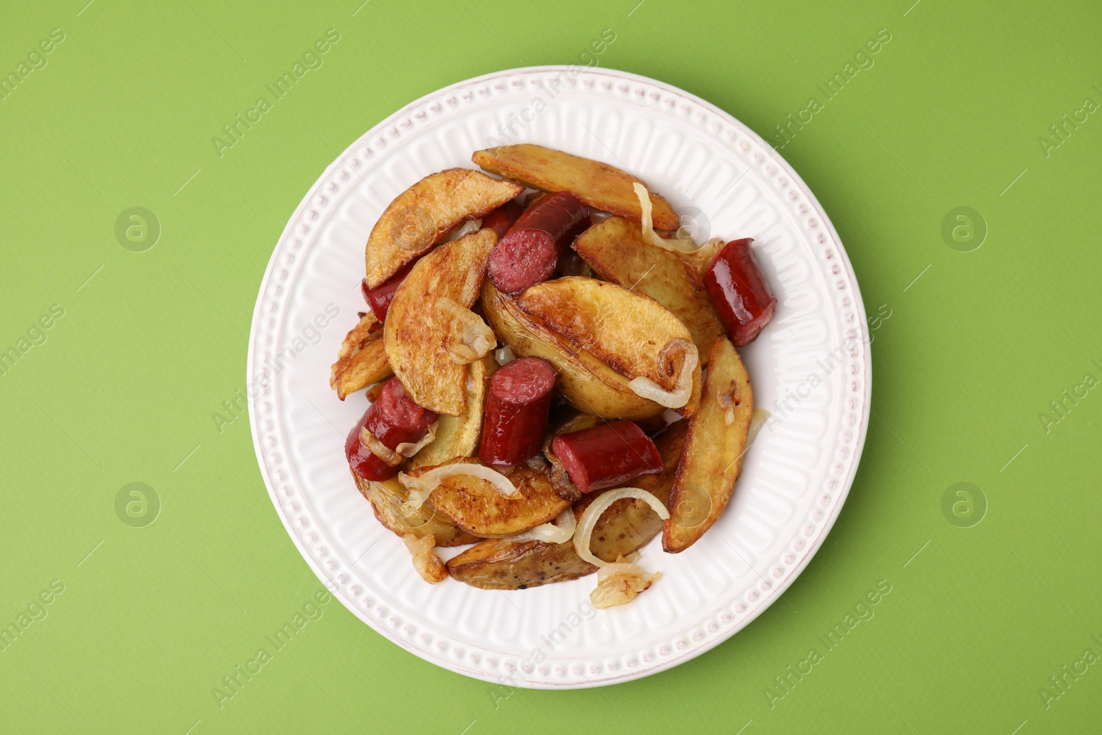 Photo of Delicious baked potato with thin dry smoked sausages and onion on green table, top view