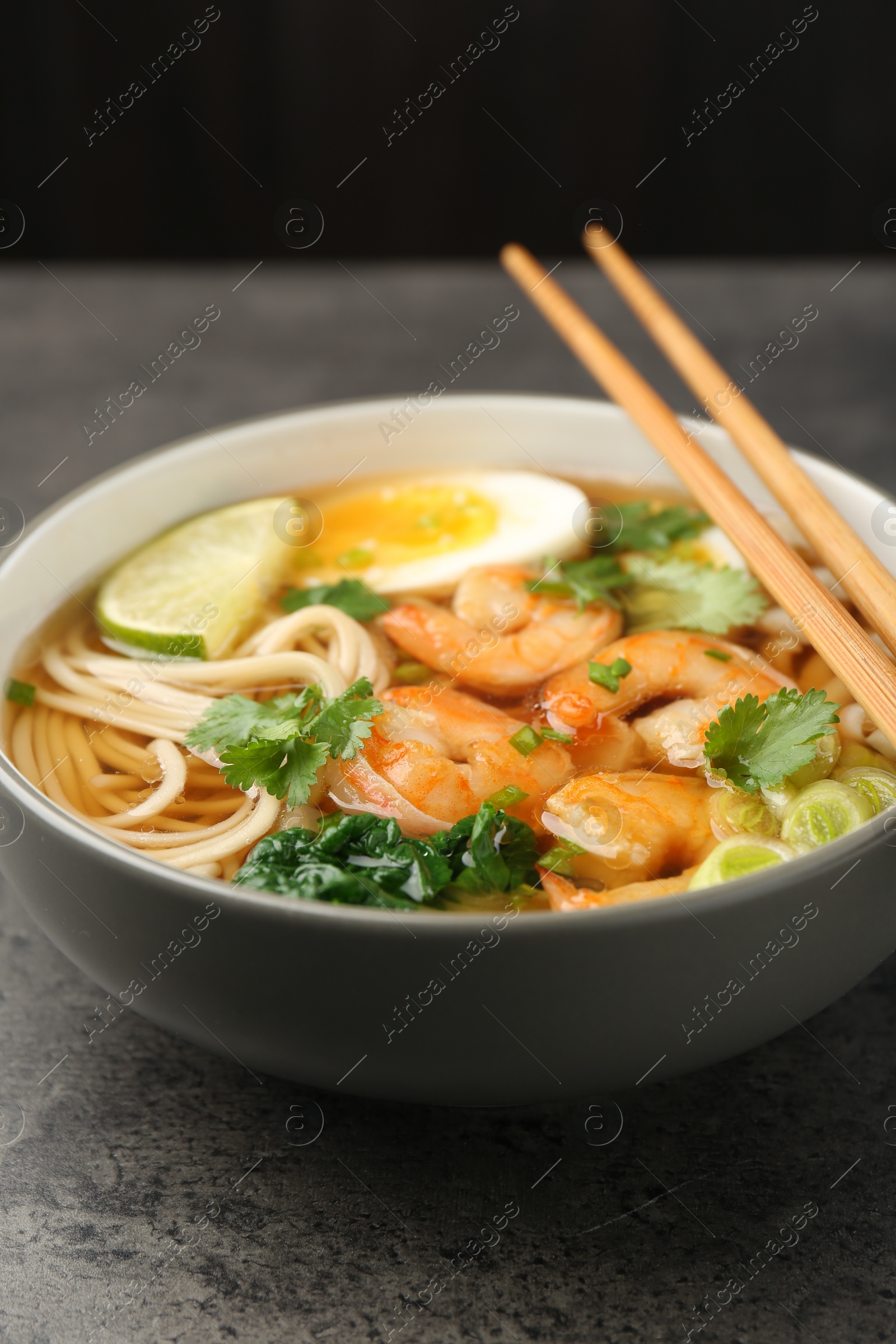 Photo of Delicious ramen with shrimps and chopsticks on grey table, closeup. Noodle soup