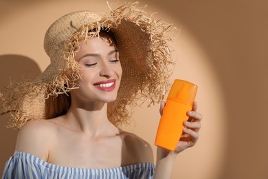 Photo of Beautiful young woman in sunlight holding sun protection cream on beige background, space for text