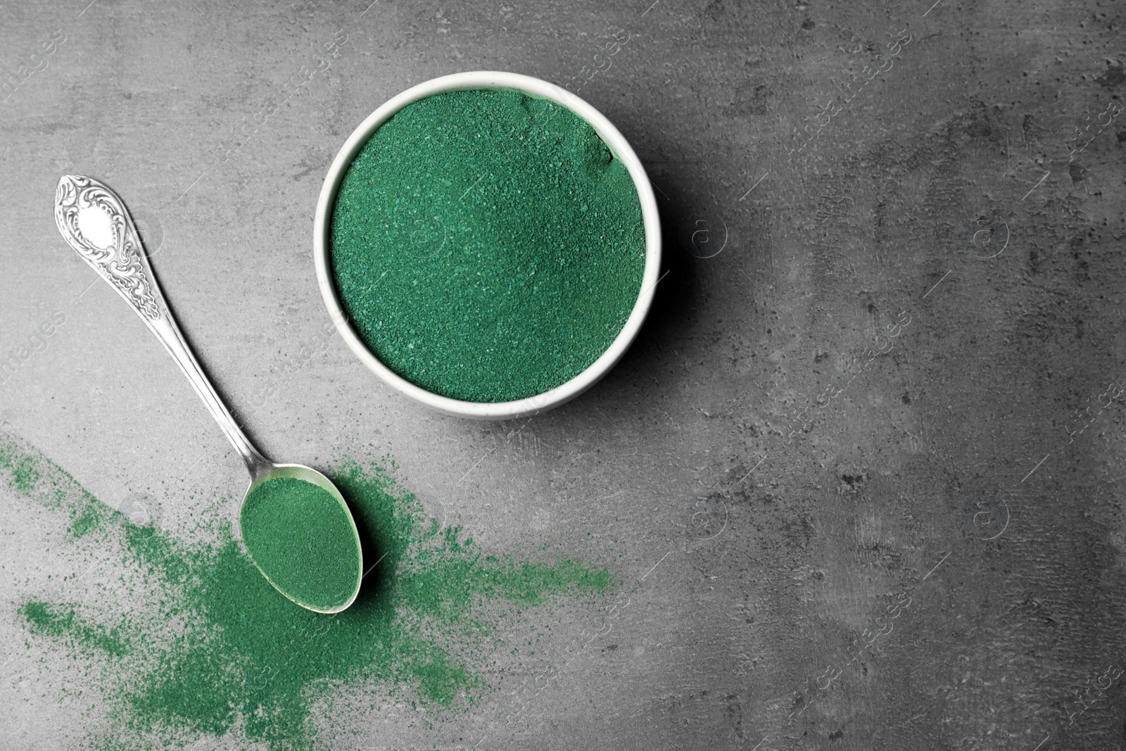 Photo of Bowl and spoon with spirulina algae powder on grey background, top view. Space for text