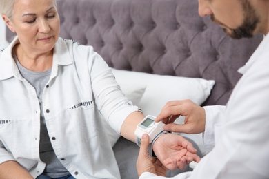 Doctor checking mature woman's pulse with medical device in bedroom