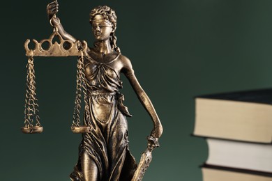 Photo of Statue of Lady Justice near books on green background, closeup and space for text. Symbol of fair treatment under law