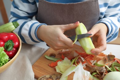 Photo of Woman peeling fresh zucchini with knife at white table, closeup