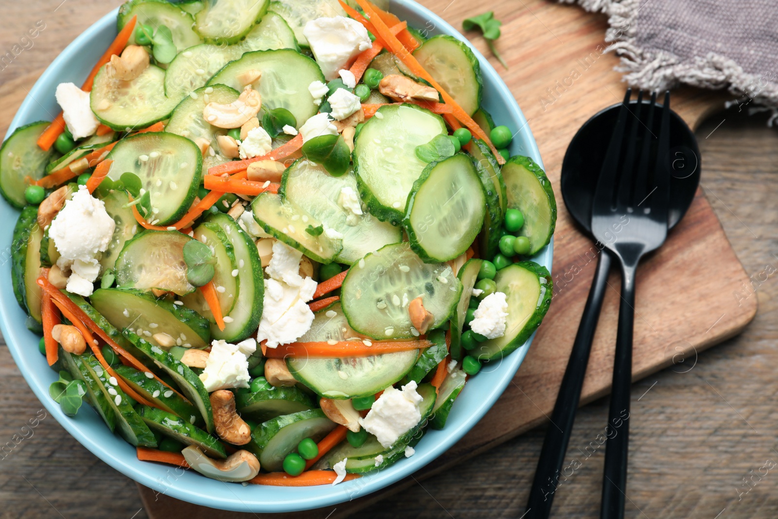 Photo of Bowl of delicious cucumber salad served on wooden table, flat lay