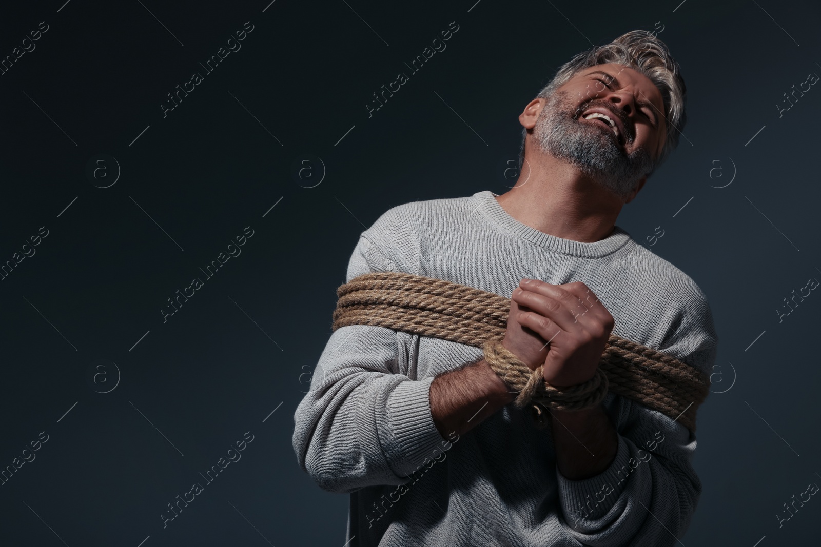 Photo of Emotional victim tied with rope on dark background, space for text. Hostage taking