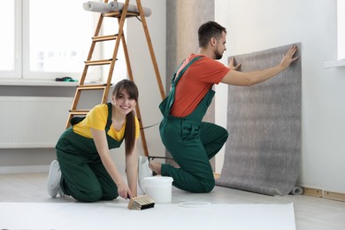 Photo of Workers hanging stylish gray wallpaper in room