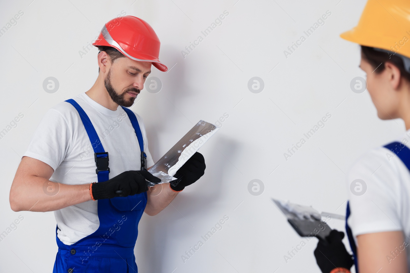 Photo of Professional workers with putty knives in hard hats near wall