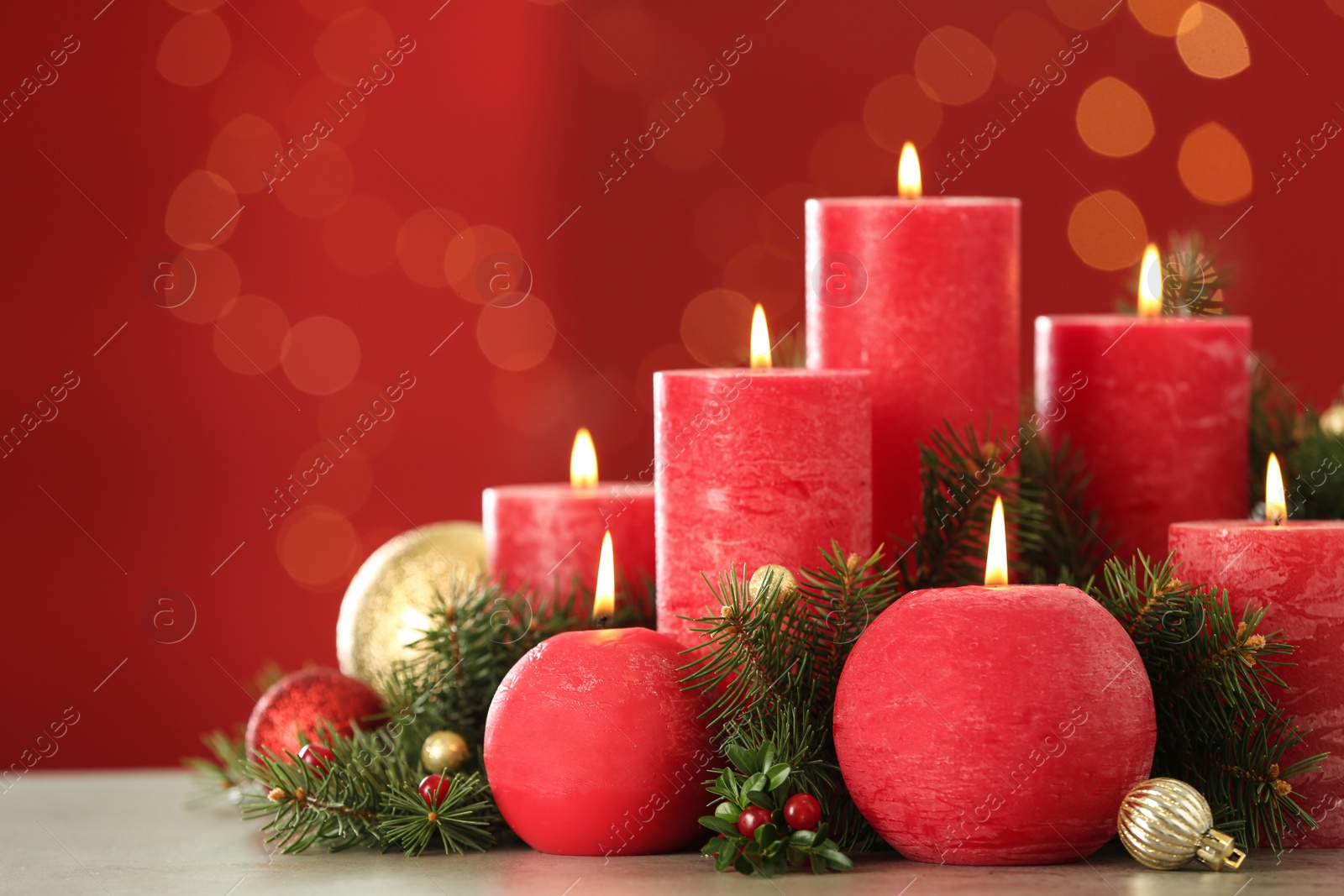 Photo of Burning candles and Christmas decor on table against red background with bokeh effect