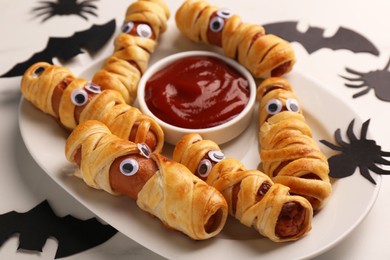 Photo of Plate with tasty sausage mummies, Halloween decorations and ketchup on white table, closeup