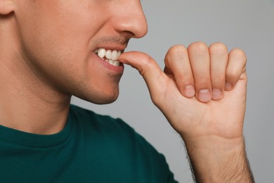 Photo of Man biting his nails on grey background, closeup. Bad habit