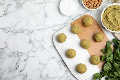 Photo of Raw falafel balls and ingredients on white marble table, flat lay. Space for text