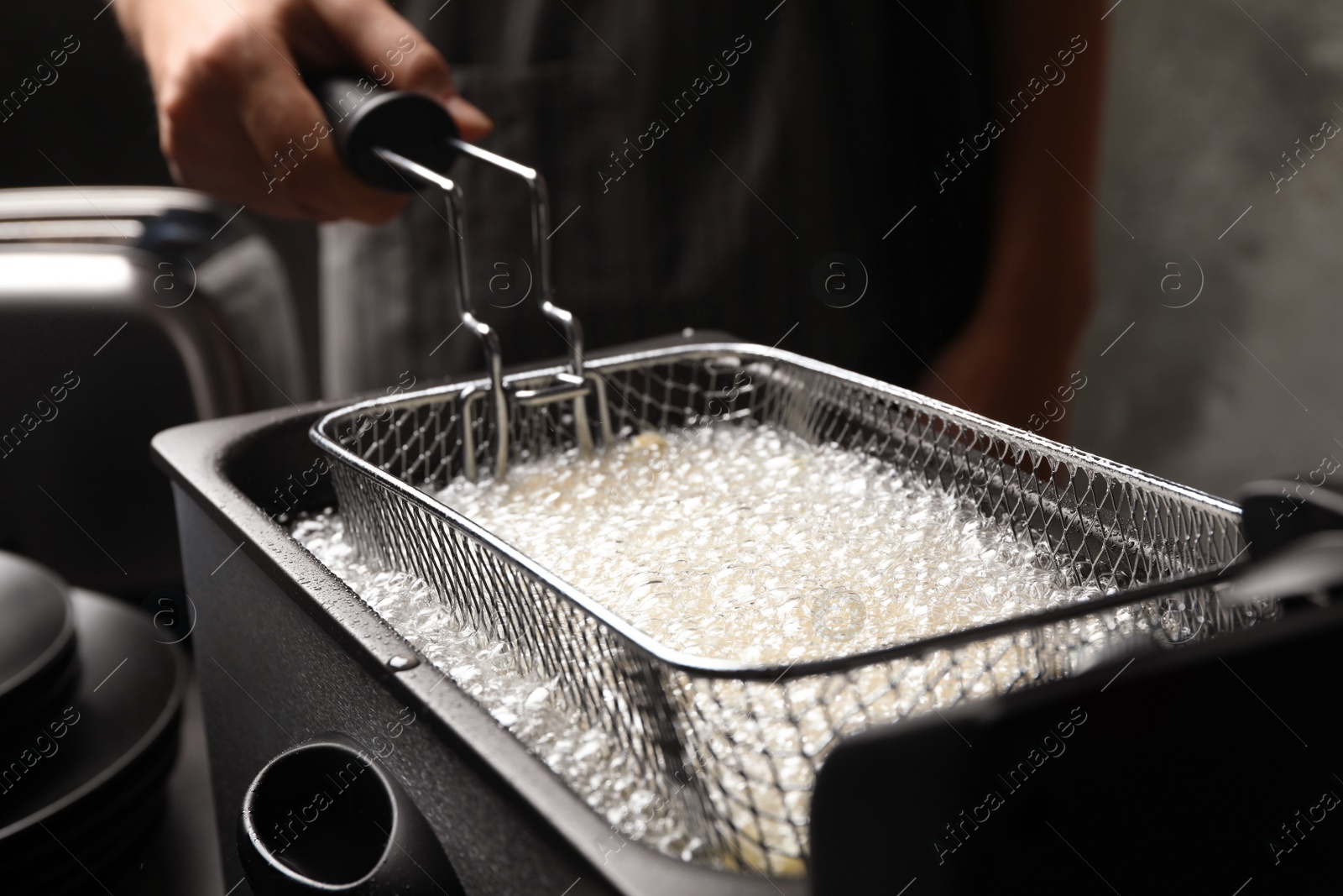 Photo of Chef cooking delicious french fries in hot oil, closeup