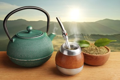 Image of Calabash with mate tea, bombilla and teapot on wooden table and beautiful view of mountain landscape