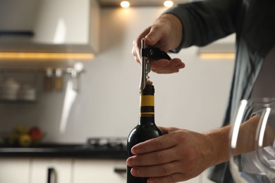 Man opening wine bottle with corkscrew indoors, closeup. Space for text