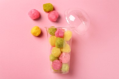 Photo of Plastic cup with color cotton balls on pink background, flat lay. Sweet candy
