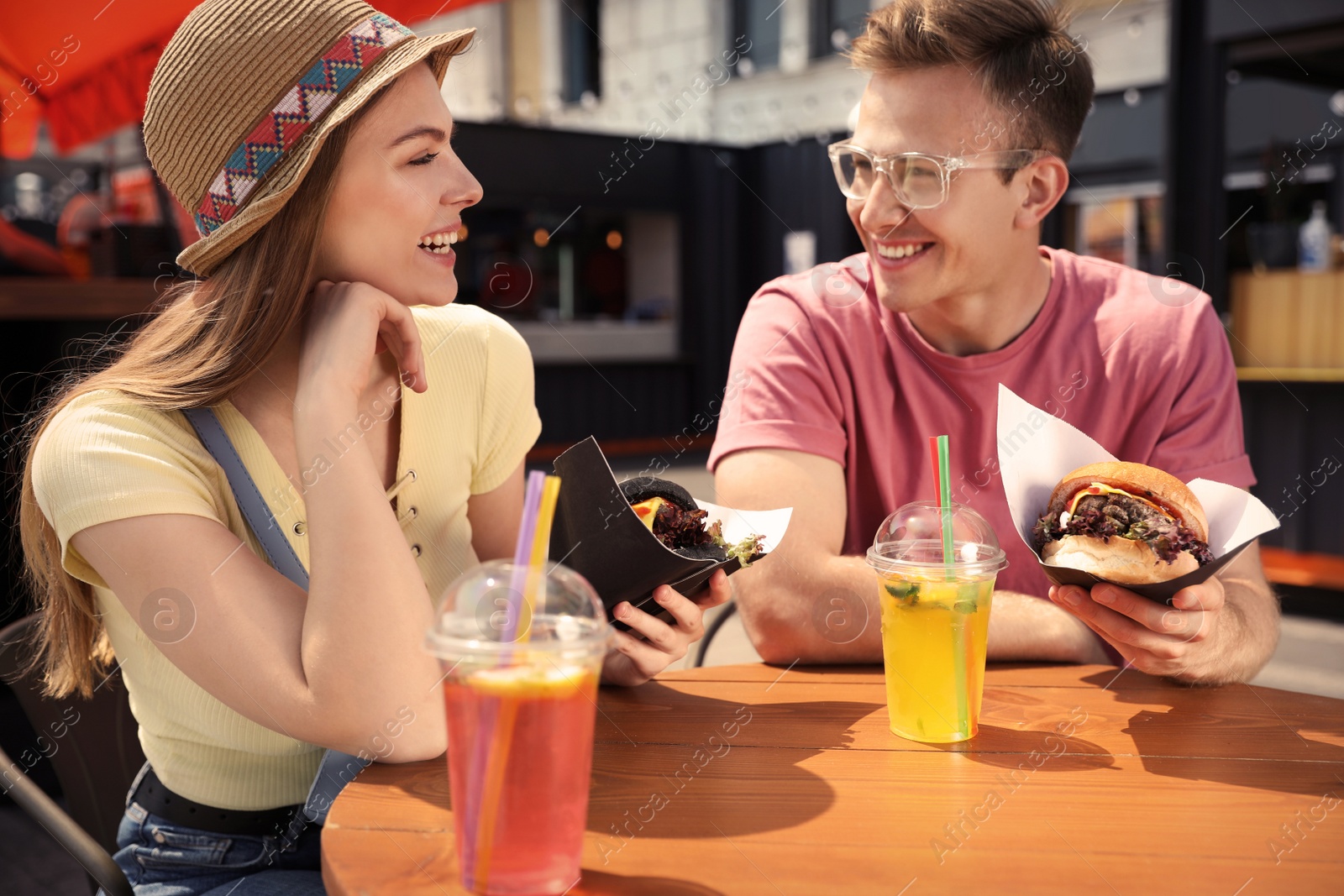 Photo of Young happy couple with burgers in street cafe