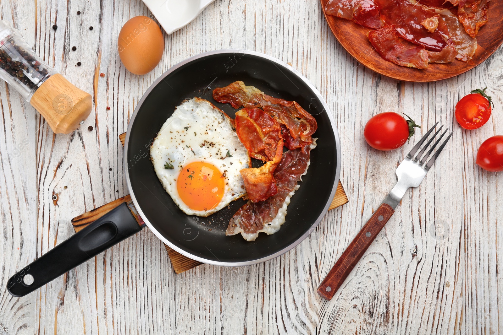 Photo of Frying pan with fried egg and bacon on wooden background
