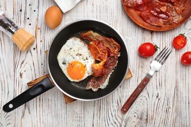 Frying pan with fried egg and bacon on wooden background