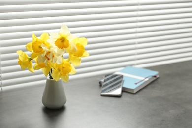 Photo of Beautiful narcissus flowers in vase near window with blinds. Space for text