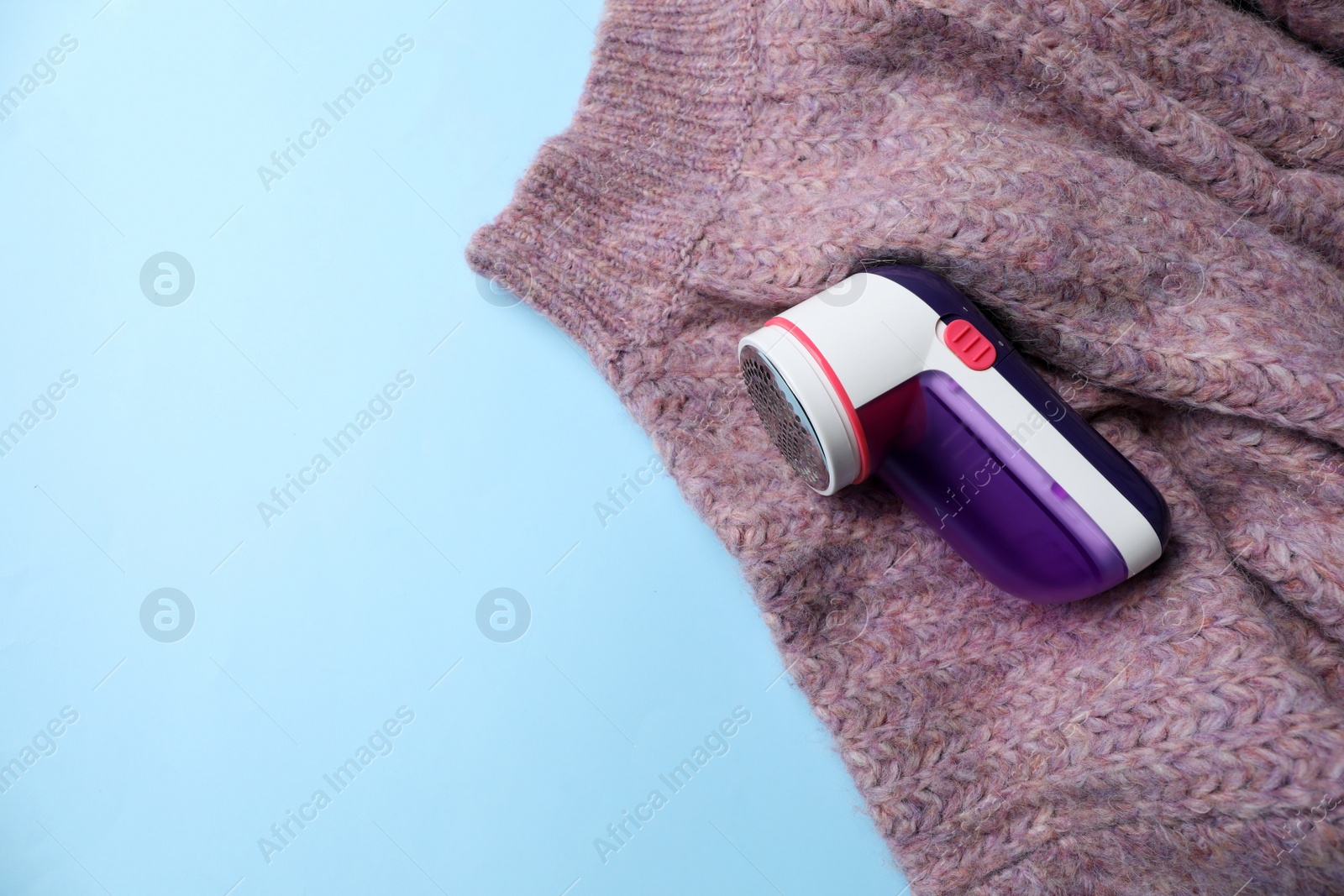 Photo of Modern fabric shaver and woolen sweater on light blue background, top view. Space for text