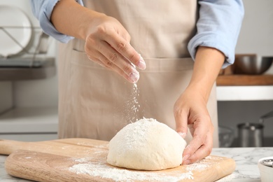 Woman sprinkling dough for pastry with flour on table