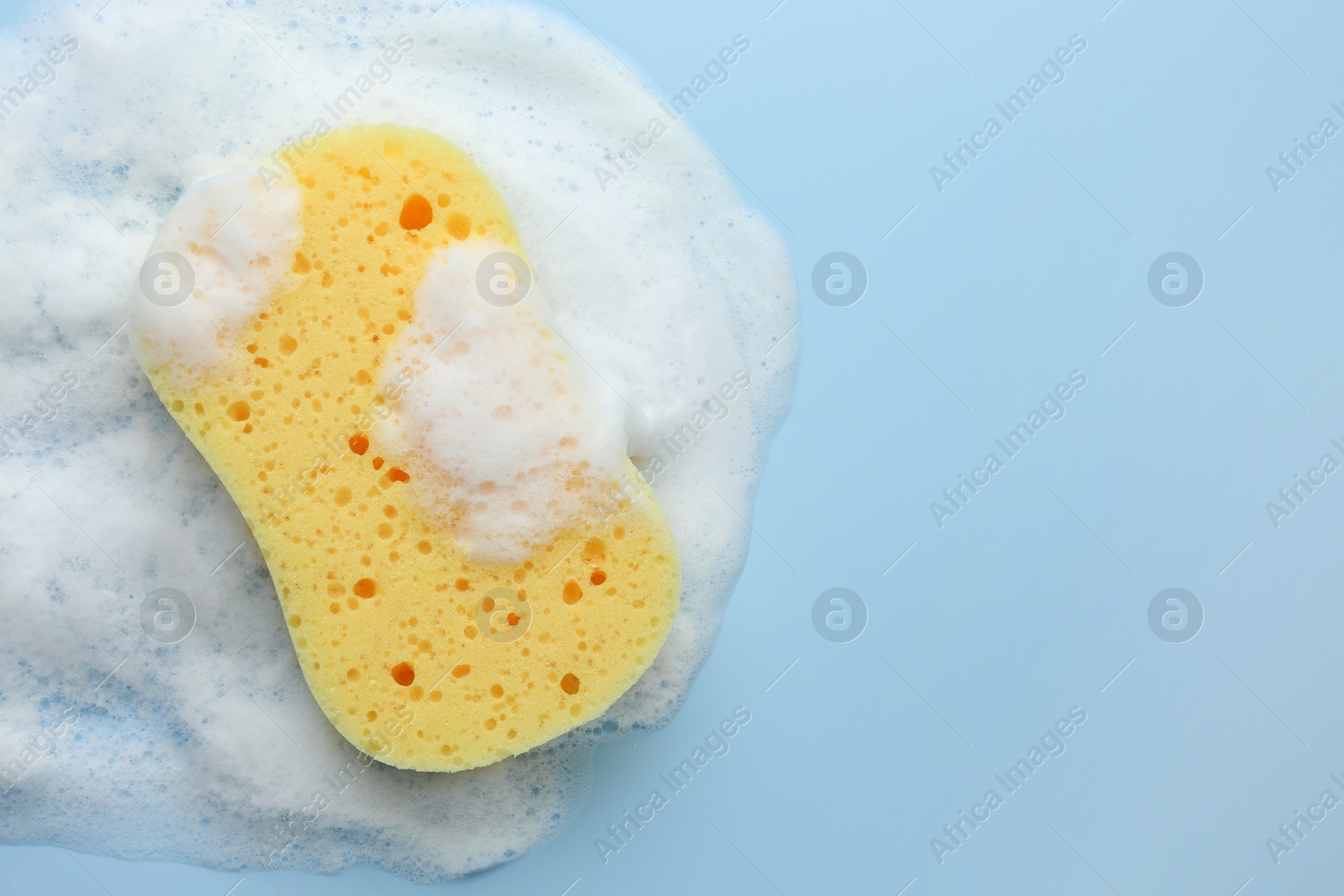Photo of Yellow sponge with foam on light blue background, top view. Space for text