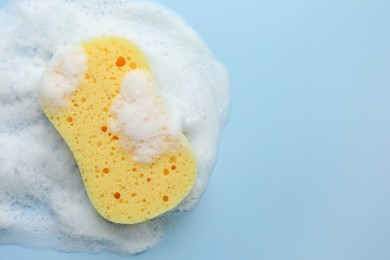 Yellow sponge with foam on light blue background, top view. Space for text