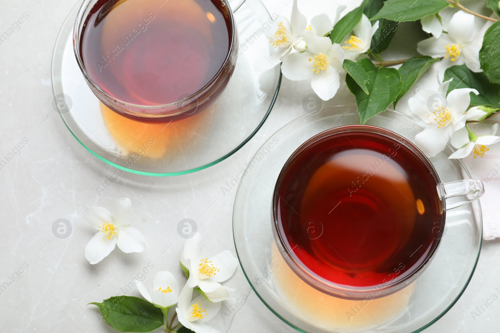 Photo of Cups of tea and fresh jasmine flowers on light grey marble table, flat lay