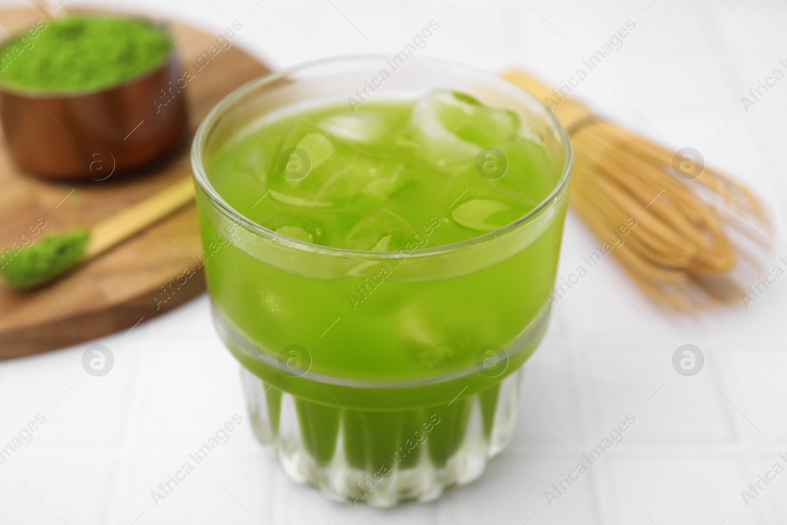 Photo of Glass of delicious iced green matcha tea on white tiled table, closeup