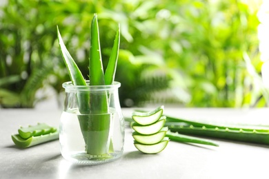 Jar with fresh aloe vera leaves on table against blurred background. Space for text