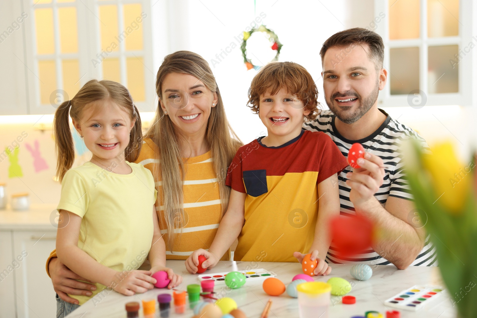 Photo of Easter celebration. Portrait of happy family with painted eggs at white marble table in kitchen