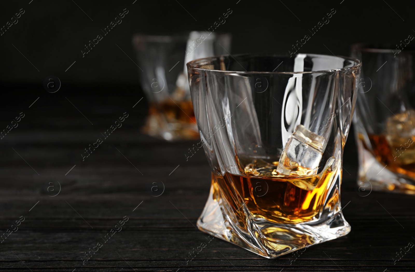 Photo of Golden whiskey in glass with ice cubes on wooden table. Space for text