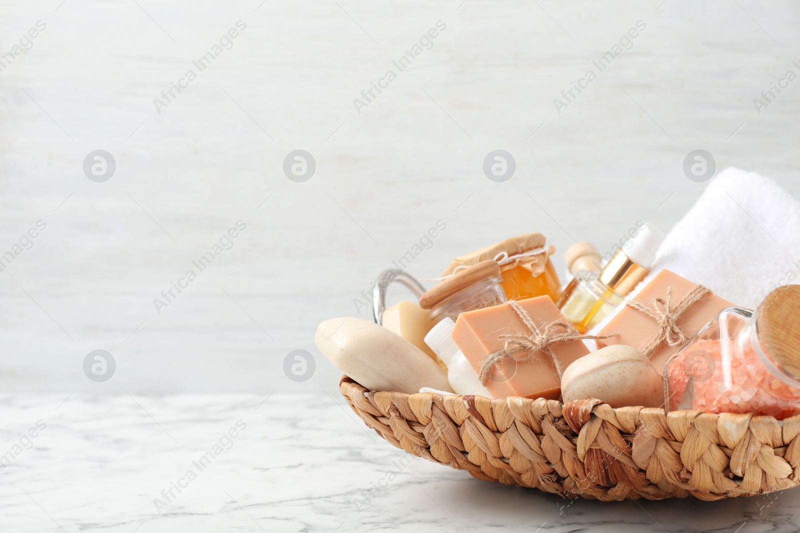 Photo of Basket with different soap bars and bath accessories on marble table. Space for text