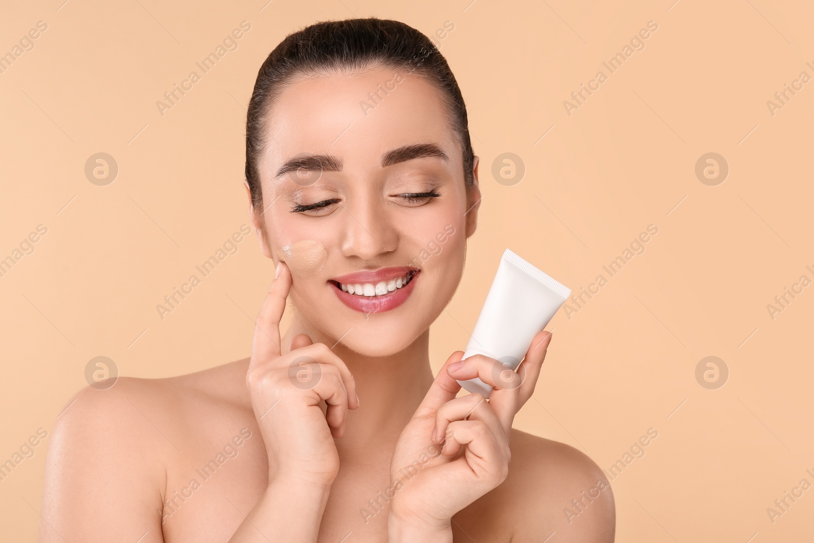 Photo of Woman holding tube of foundation on beige background. Space for text