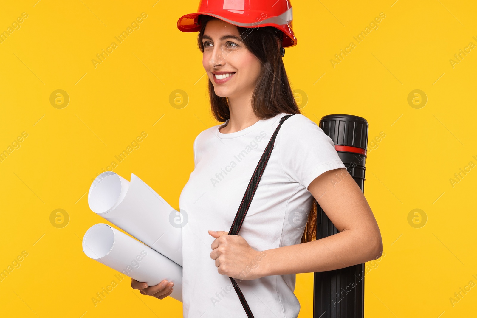 Photo of Architect in hard hat with drafts and tube on yellow background