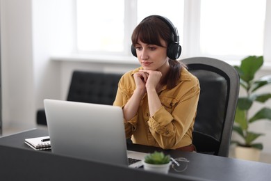 Woman in headphones watching webinar at table in office